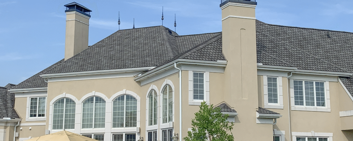 large tan colored custom home sitting beneath blue sky with some white clouds