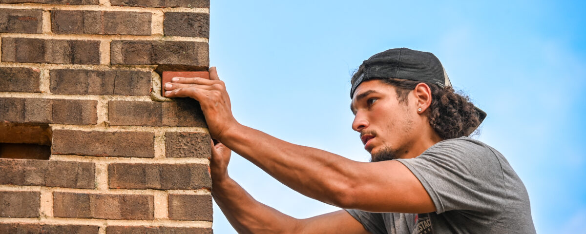 chimney professional working on the exterior of a chimney with blue sky behind him