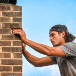 chimney professional working on the exterior of a chimney with blue sky behind him