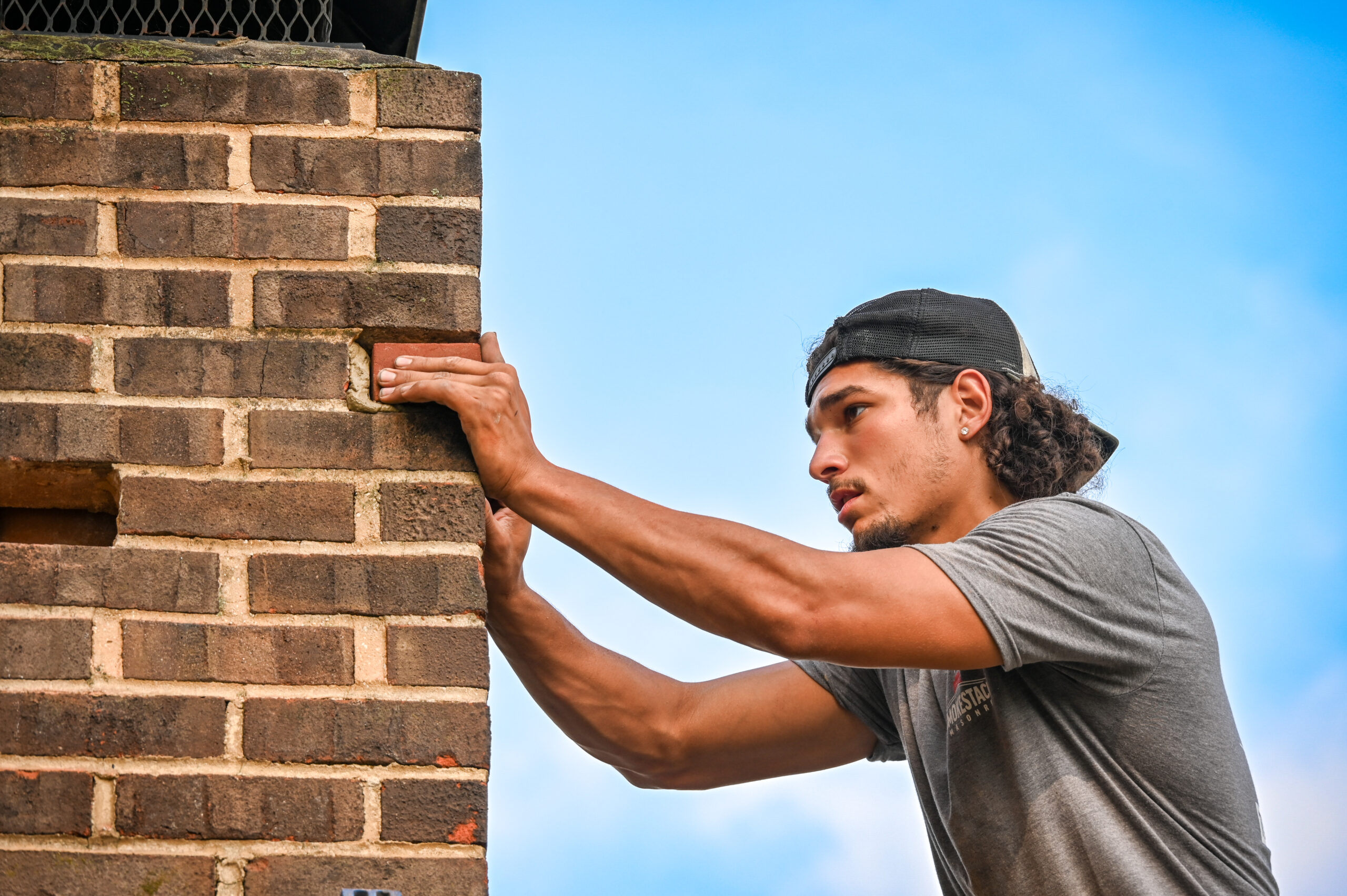 chimney professional working on the exterior of a chimney with blue sky behind him